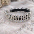 A silver rhinestone-embellished collar with black elastic bands, displayed on a white faux fur surface with scattered clear rhinestones.