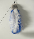 A blue and white feather toy with a gray fluffy pom-pom top and metal hanging clip, shown against a plain off-white wall.