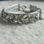 A silver-toned collar embellished with clear marquise and oval rhinestones, resting on a textured white fabric surface.