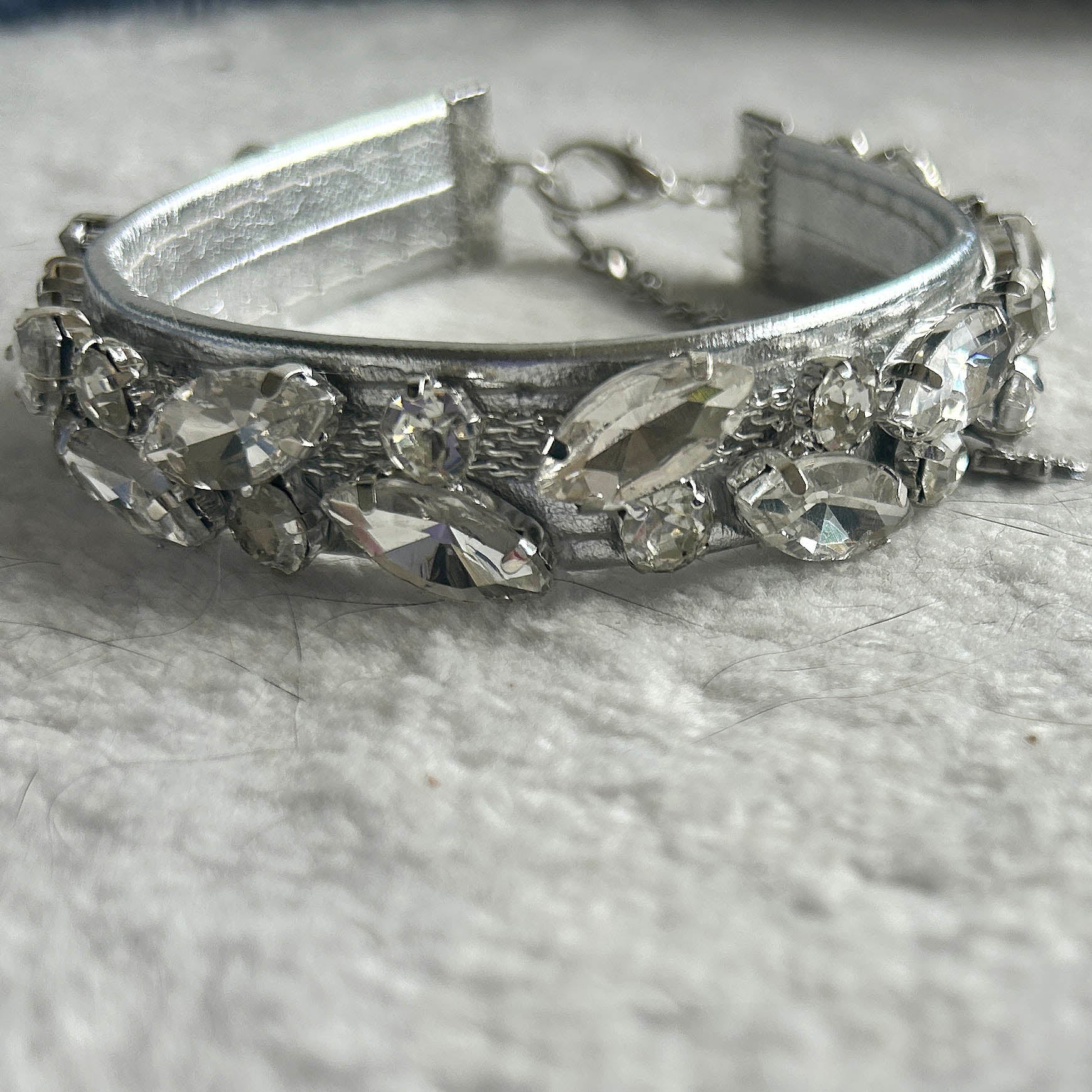 A silver-toned collar embellished with clear marquise and oval rhinestones, resting on a textured white fabric surface.