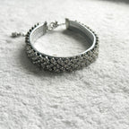 A silver-toned collar encrusted with clear pavé stones, resting on a textured white fabric background.