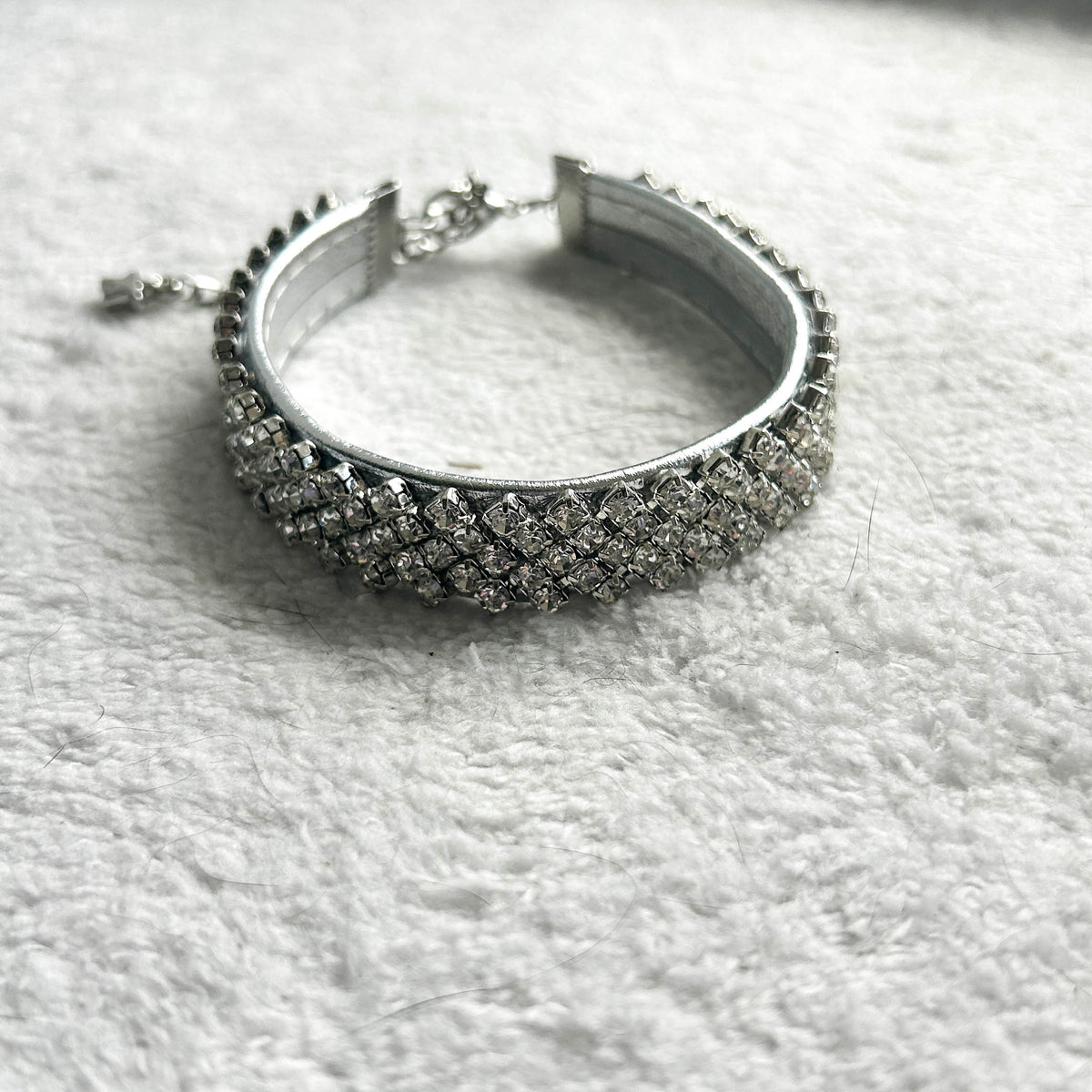 A silver-toned collar encrusted with clear pavé stones, resting on a textured white fabric background.