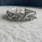 A silver-toned collar embellished with clear faceted rhinestones, resting on a textured white fabric surface.