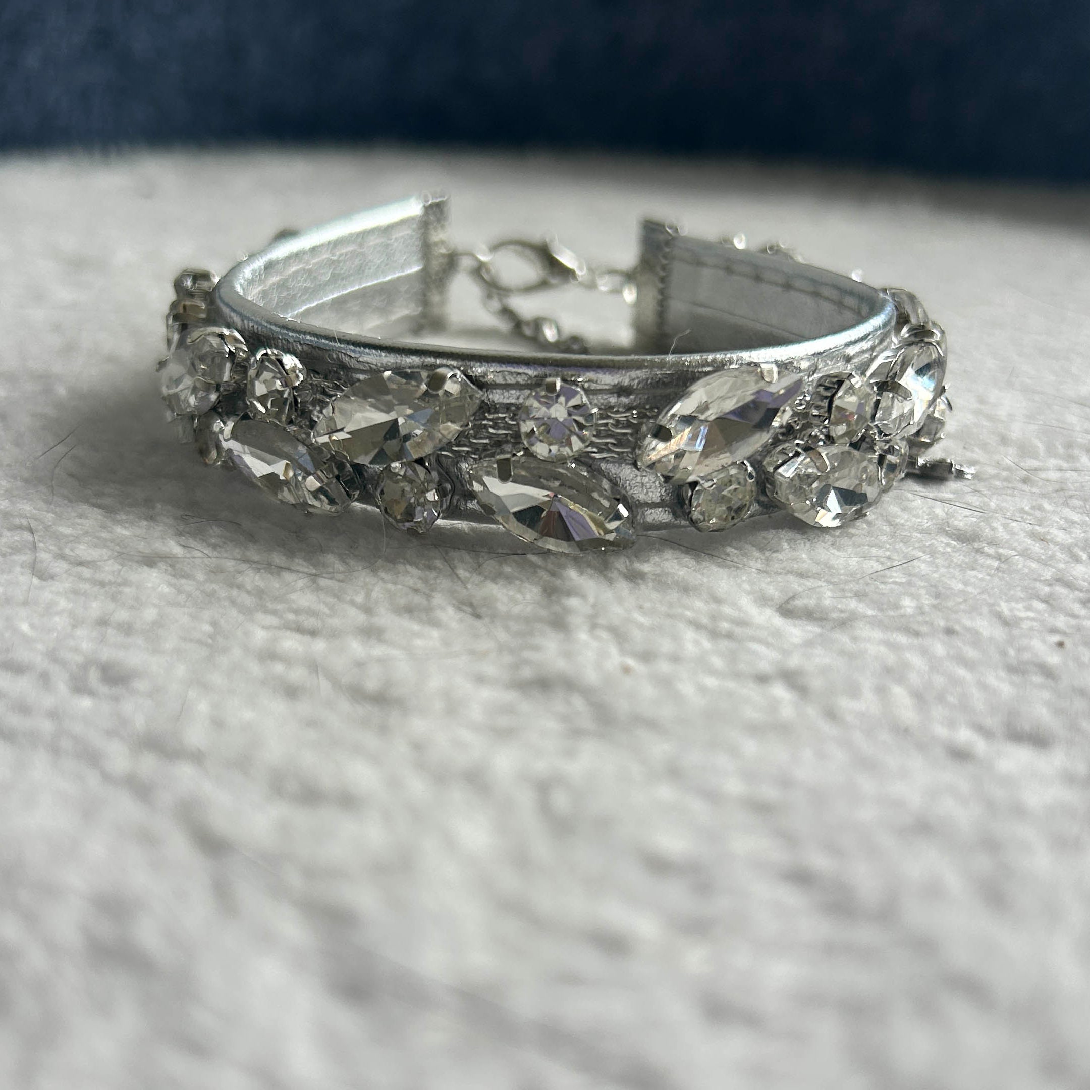 A silver-toned collar embellished with clear faceted rhinestones, resting on a textured white fabric surface.