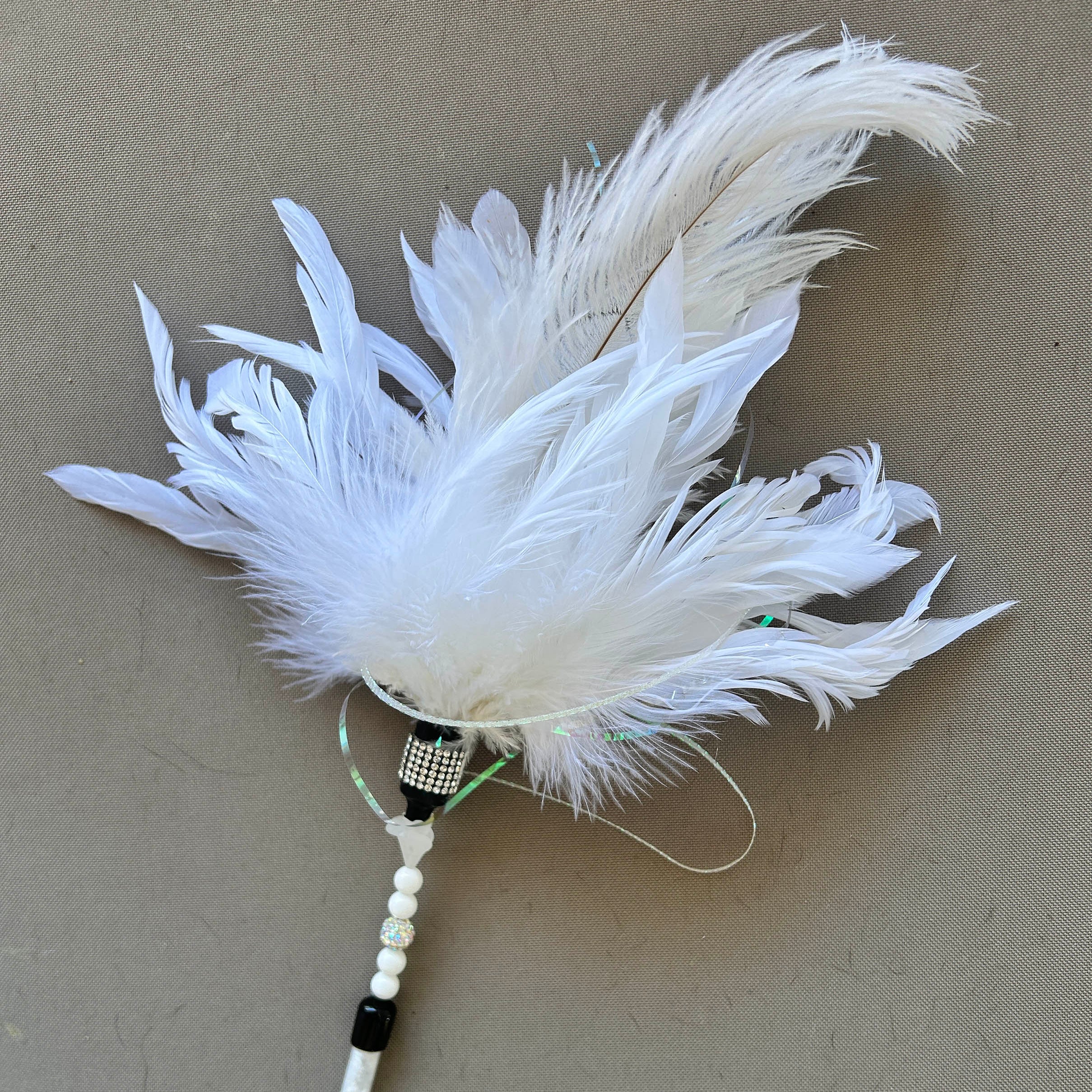 A white feather duster with a white beaded handle and black accents, photographed on a neutral gray background.