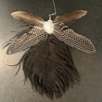A cat toy made from multiple natural feathers, including a large dark brown feather, lighter brown feathers, white speckled feathers, and a fluffy white center, photographed against a dark textured background.