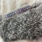 A close-up of a gray faux fur sleeve or cuff with a wide silver-toned band embellished with iridescent rhinestones, resting on a soft cream-colored faux fur surface.