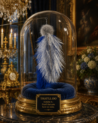 A decorative blue and white feathered cat toy under a clear glass dome on an ornate gold pedestal, with a plaque reading 'THAT'LL DO' in a richly decorated interior setting.