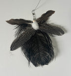 A  feather cat toy made from several dark feathers, including black and brown feathers with white speckles, a white fluffy centre, and a metal hanging loop.
