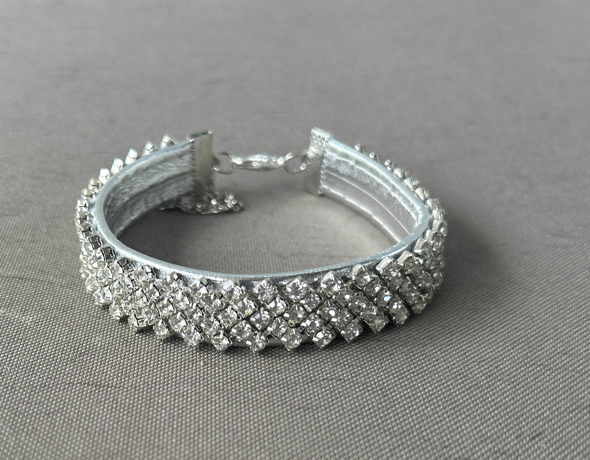 A silver-toned collar encrusted with clear rhinestones, displayed on a textured gray fabric background.