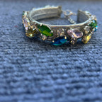 A wide collar adorned with multiple colorful rhinestones in green, blue, pink, and yellow, resting on a textured blue fabric background.