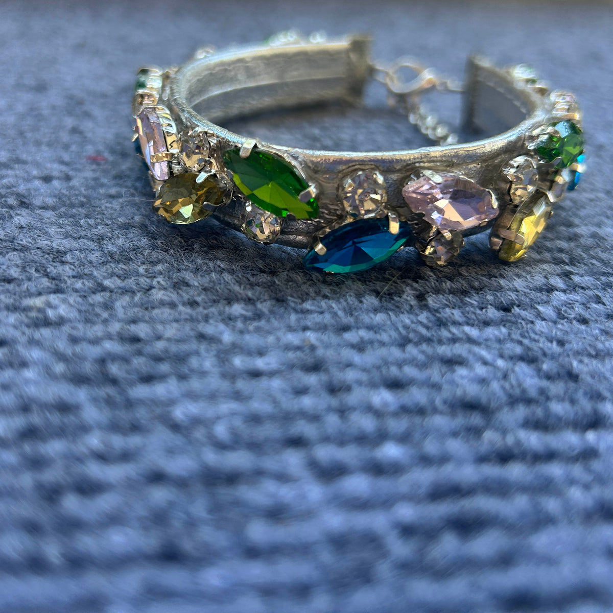 A wide collar adorned with multiple colorful rhinestones in green, blue, pink, and yellow, resting on a textured blue fabric background.