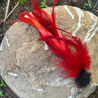 A bright red and orange feather cat lure with a thorax, resting on a textured gray stone outdoors.